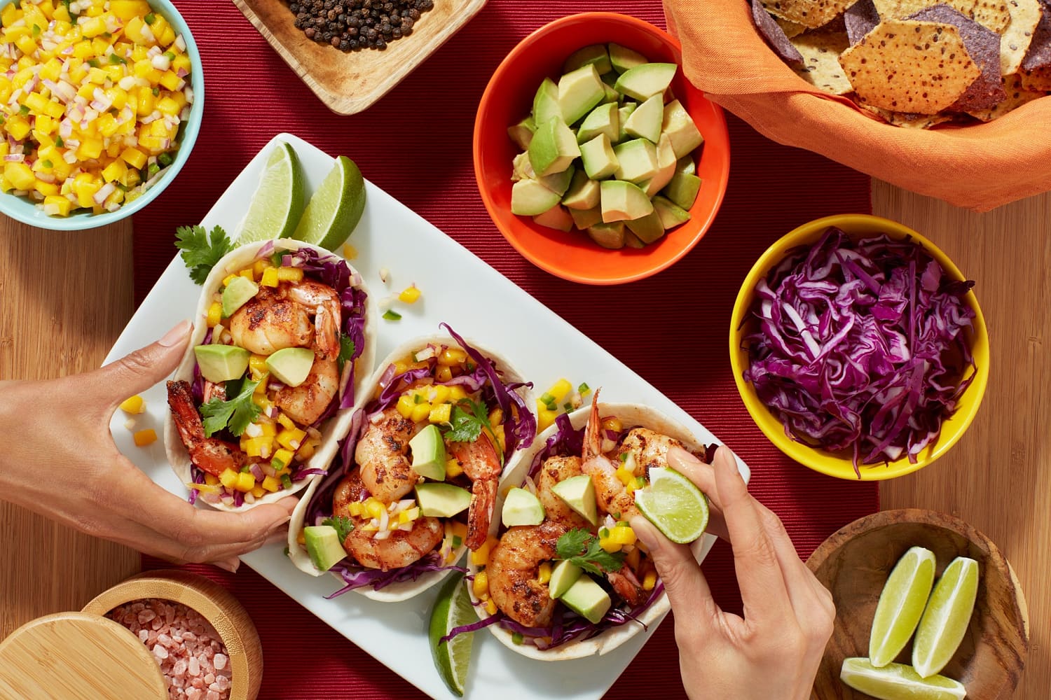 Three soft shell shrimp tacos on a white plate with surrounded by small bowls of taco toppings